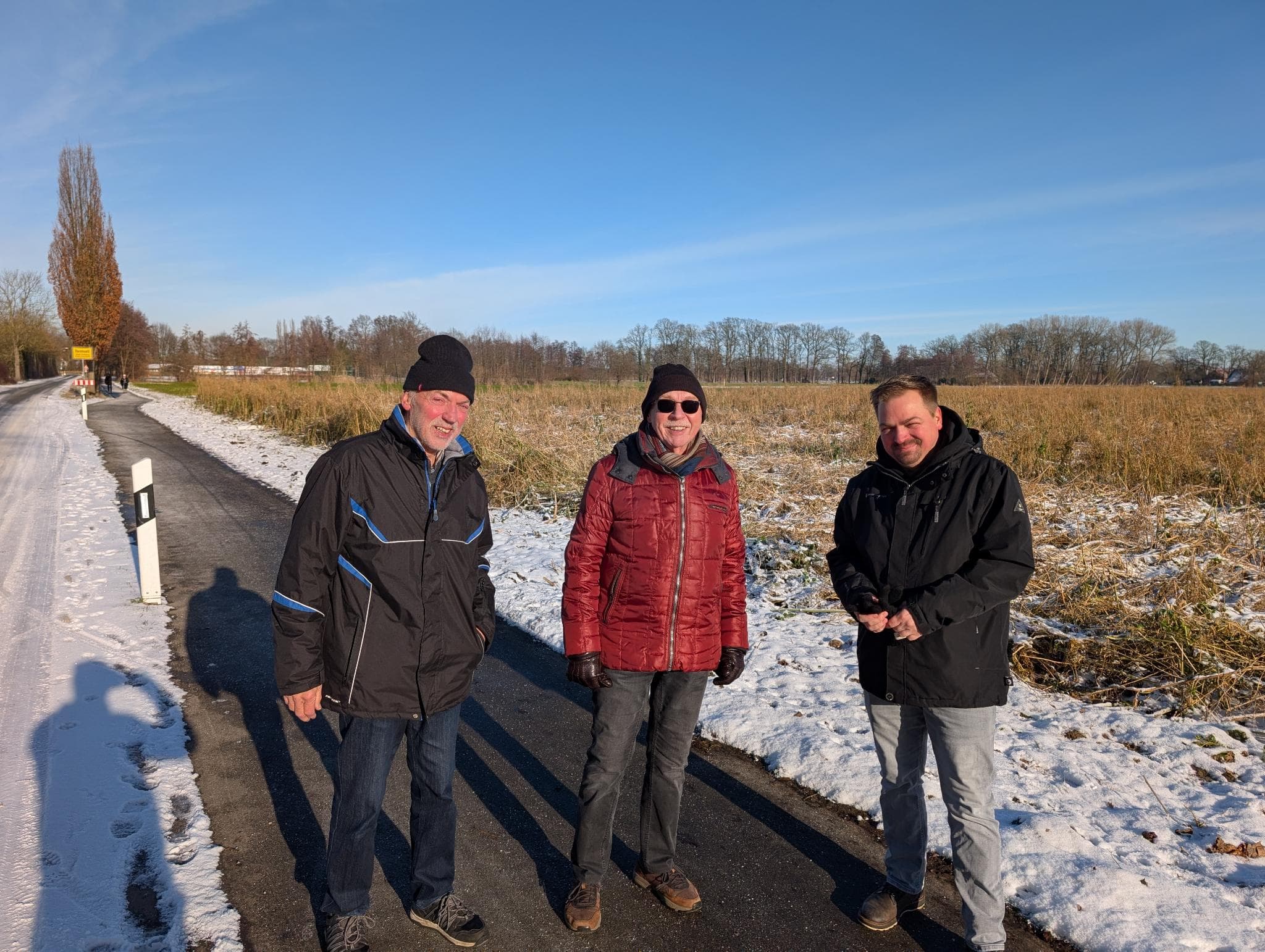 Wandergruppe auf verschneitem Feldweg unter blauem Winterhimmel